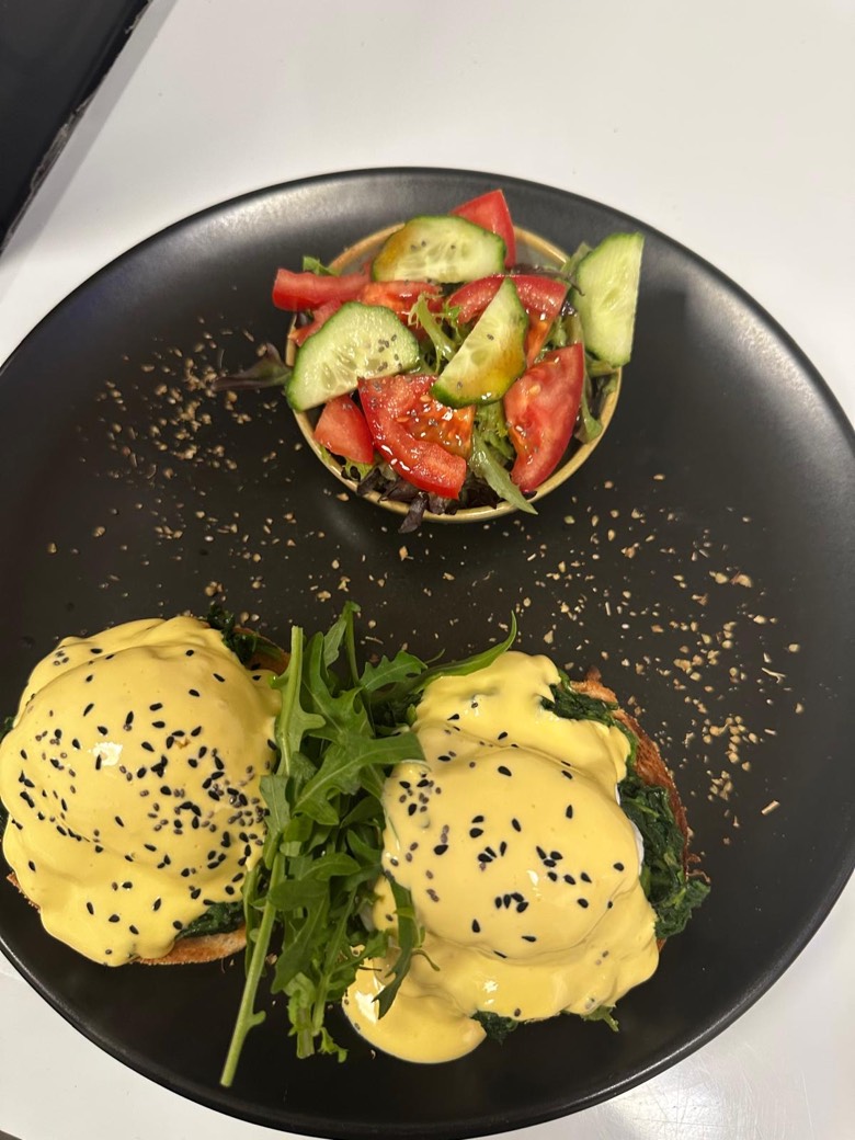 Eggs benedict with poached eggs, hollandaise and black sesame on a matte black plate