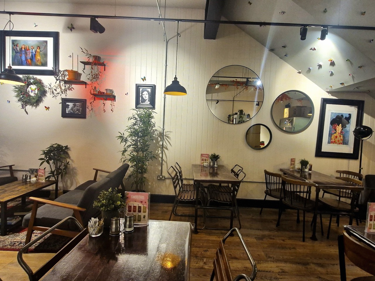 The bright back room at Mego with mid-century seating, round mirrors, framed art and hanging plants