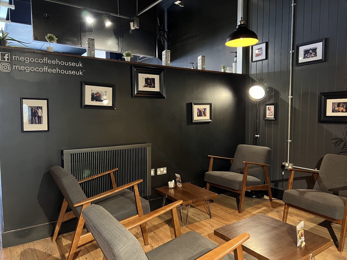A cosy corner at Mego with grey armchairs, wooden tables and framed prints on a dark wall