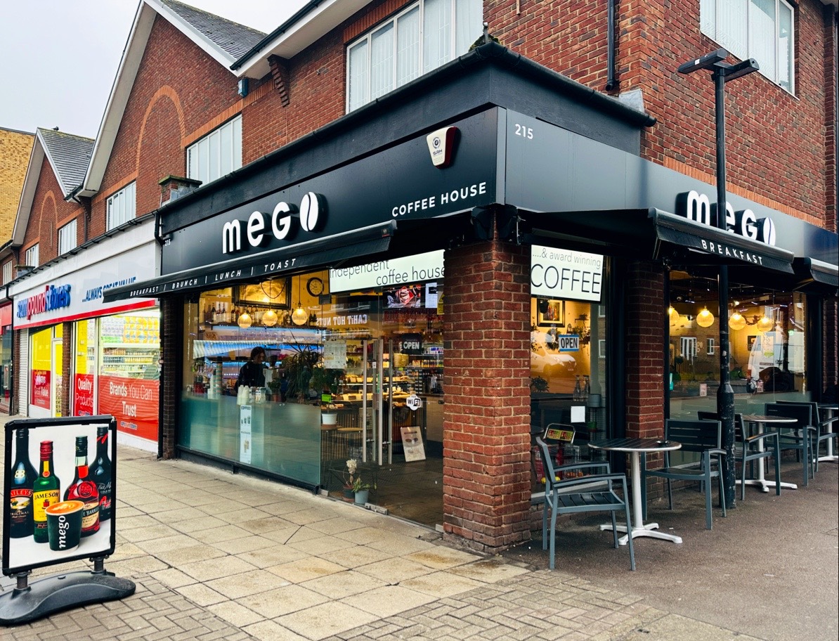 The Mego Coffee House shopfront — a black fascia with the mego wordmark on a red-brick corner unit at 215 High Street, Walthamstow, with pavement tables