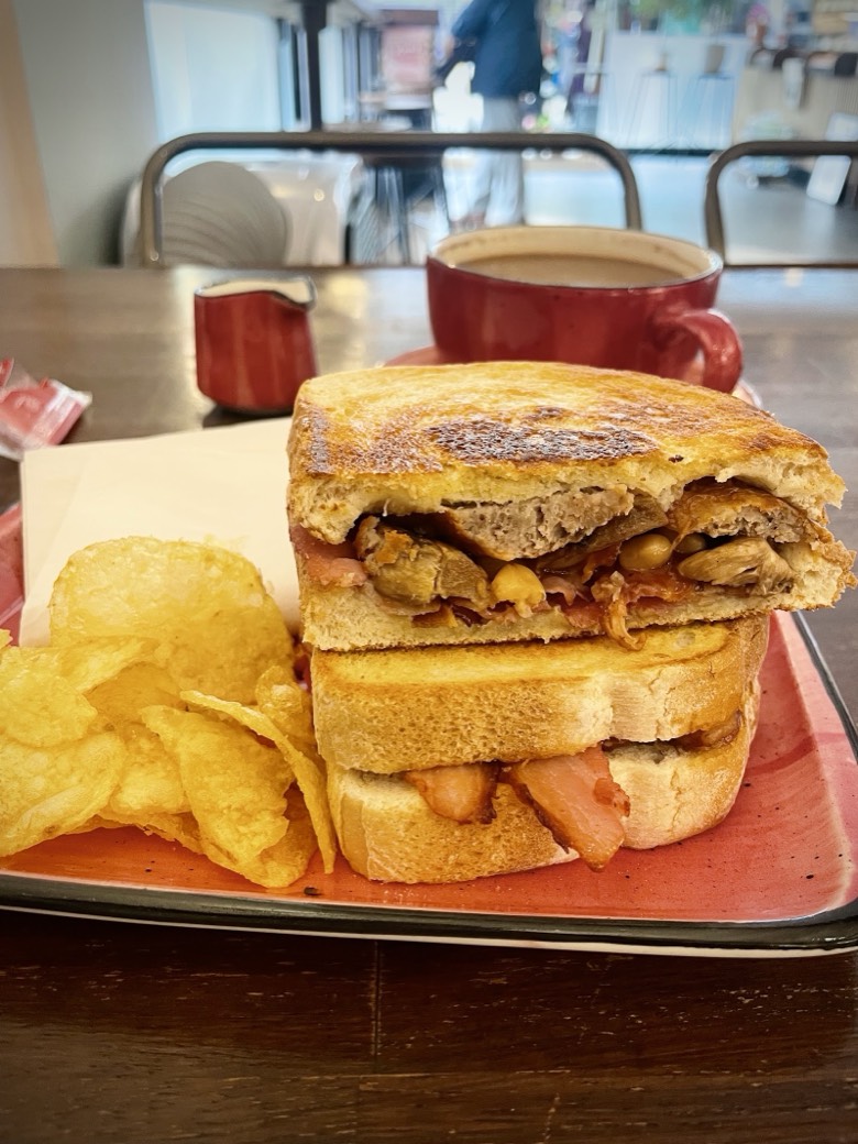A toasted club sandwich cut and stacked with a side of crisps on a terracotta plate at Mego